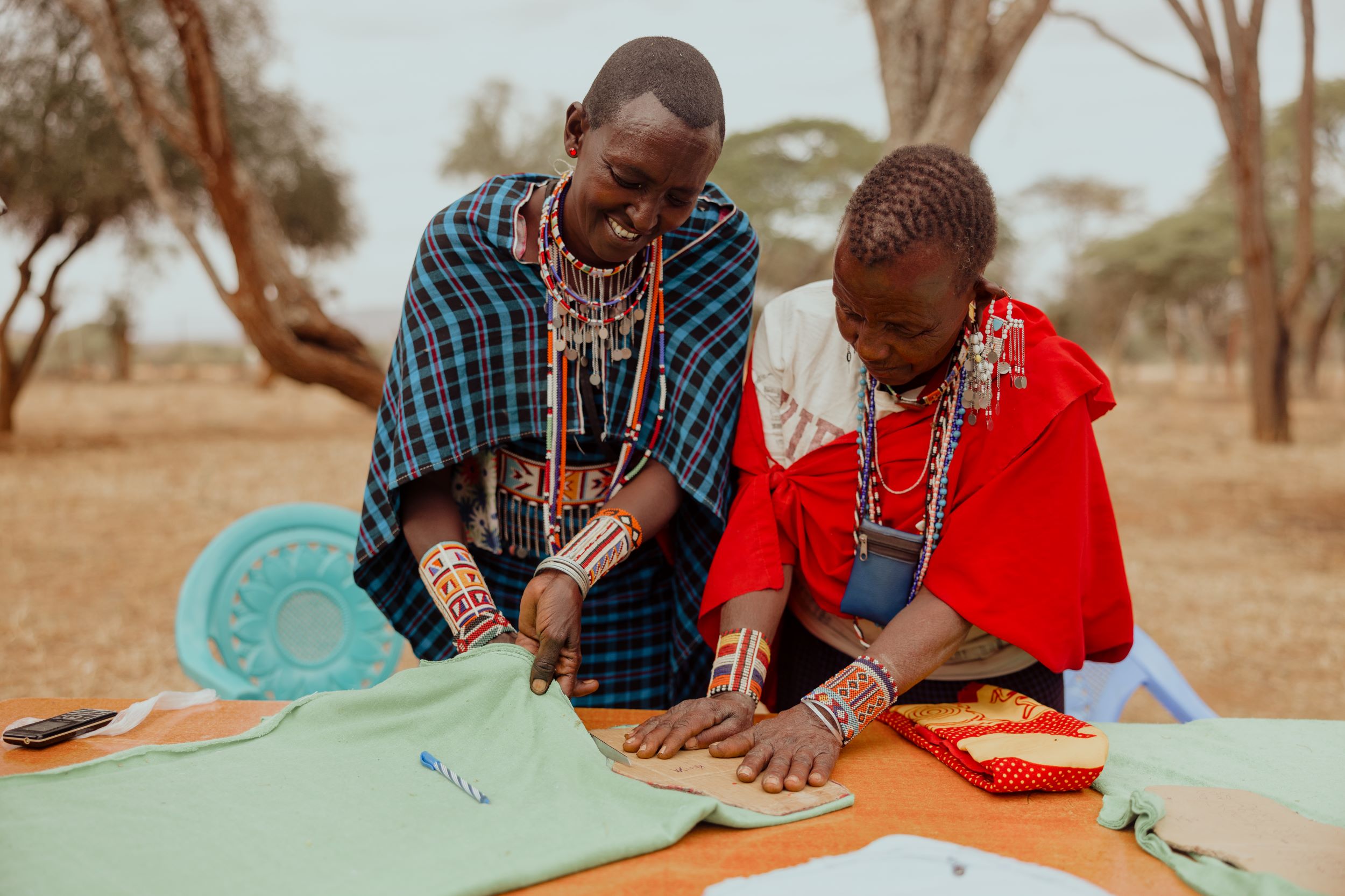 Two Kenyan women in bright traditional clothing cutting fabric together