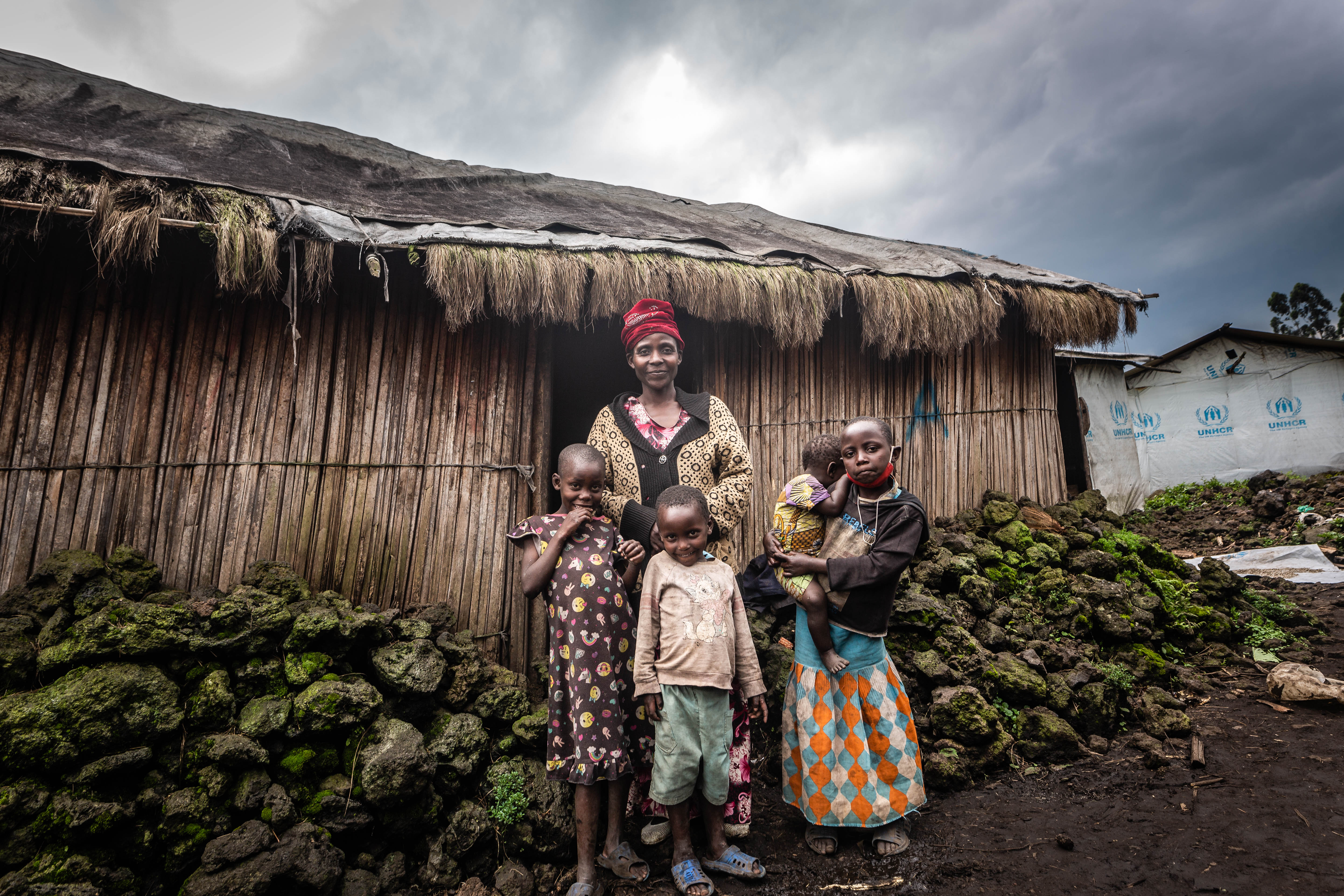 Asifiwe and her children outside their home in DRC on a cloudy day. 
