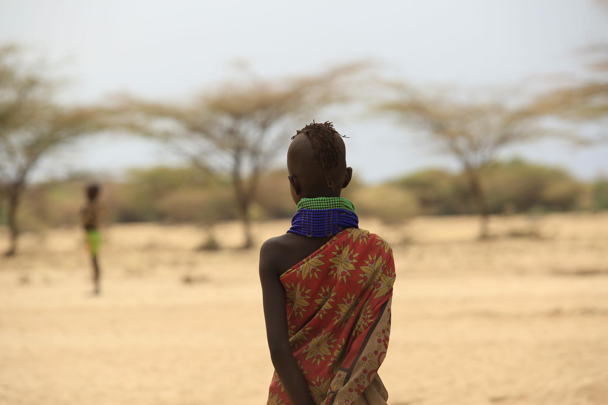 A child facing away from the camera in the middle of the empty prairie, Kenya