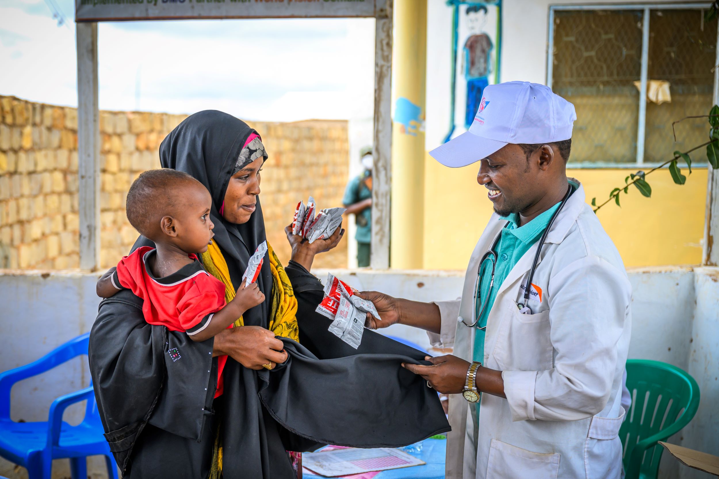 A mother holds her baby as a health worker hands over theraputic food to treat malnutrition