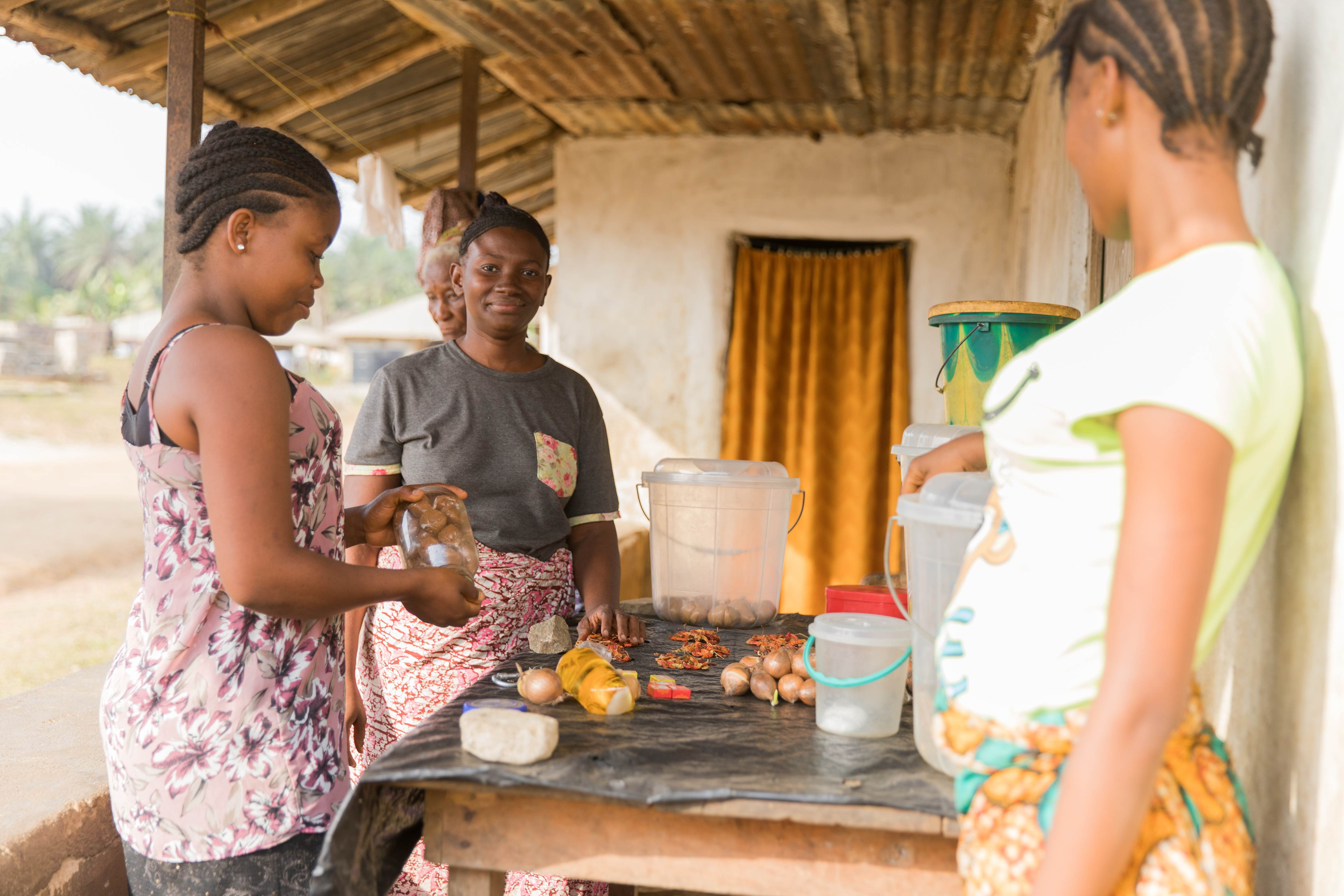 Three women from Sierra Leone stand at an outdoor shop chatting