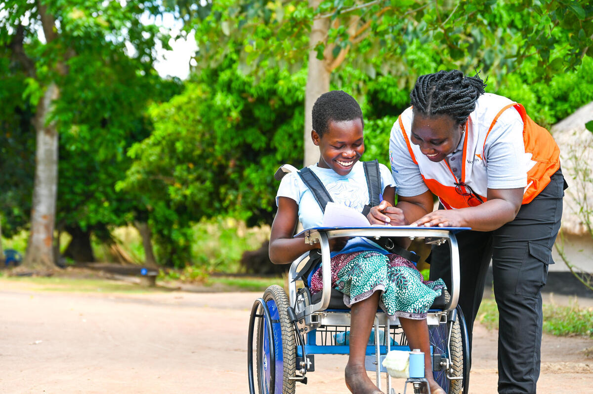 A young girl with special needs being assisted with her writing by a World Vision staff