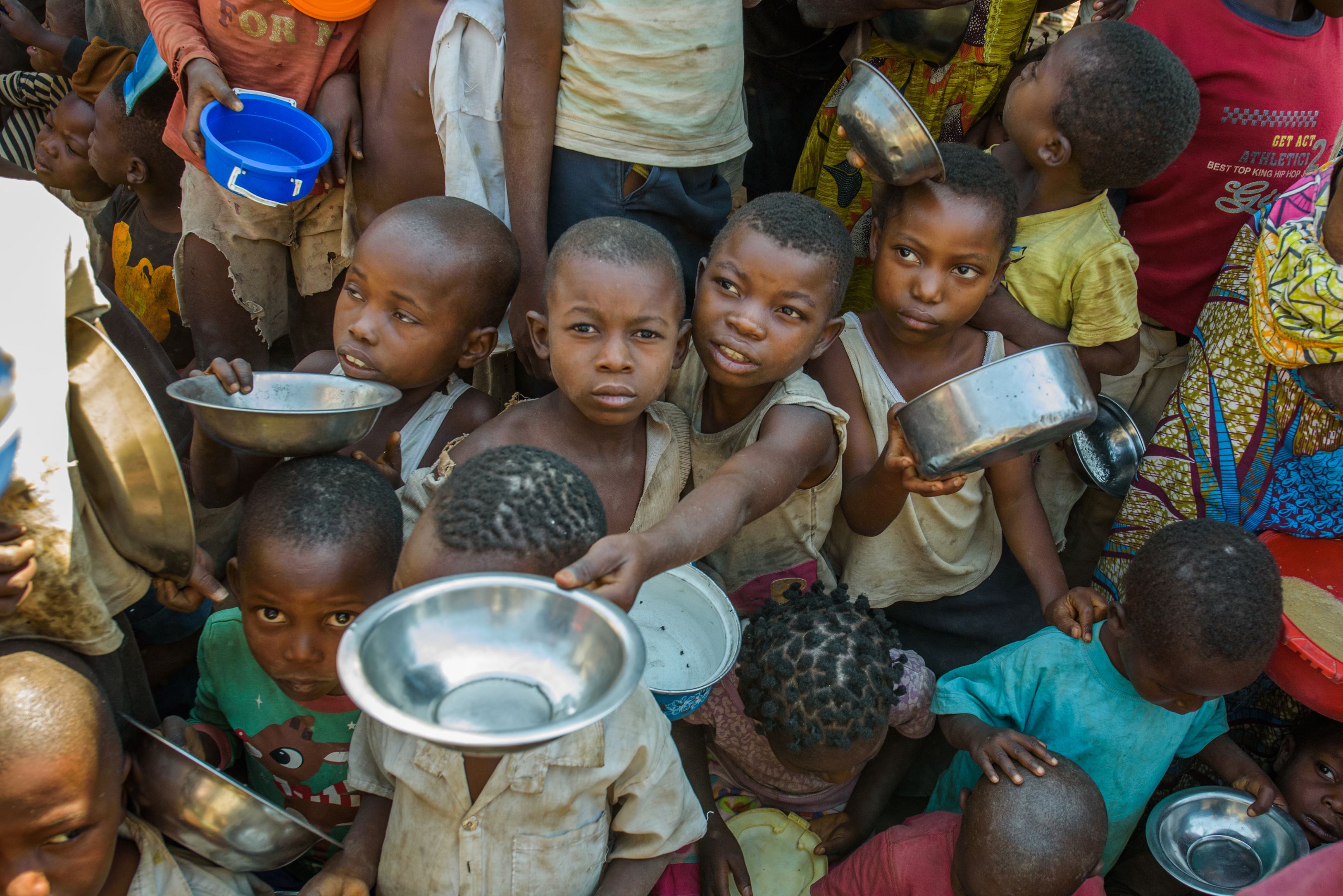 Children in DCR crowd holding out bowls to receive food to prevent malnutrition