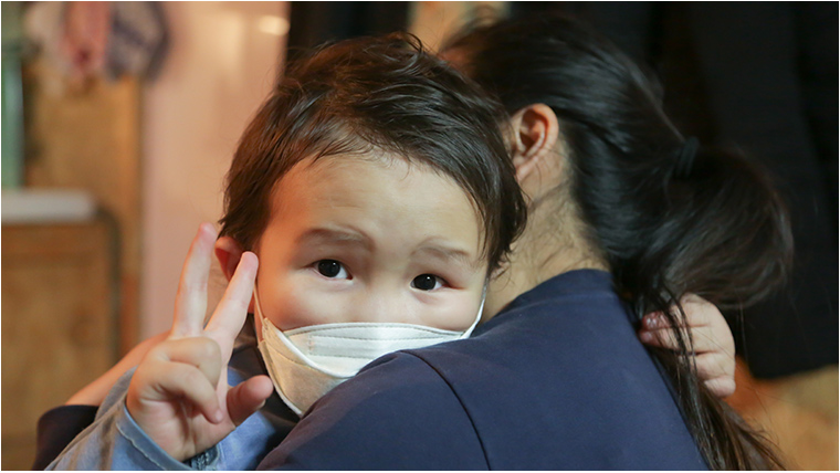Child in mask hugs adult 