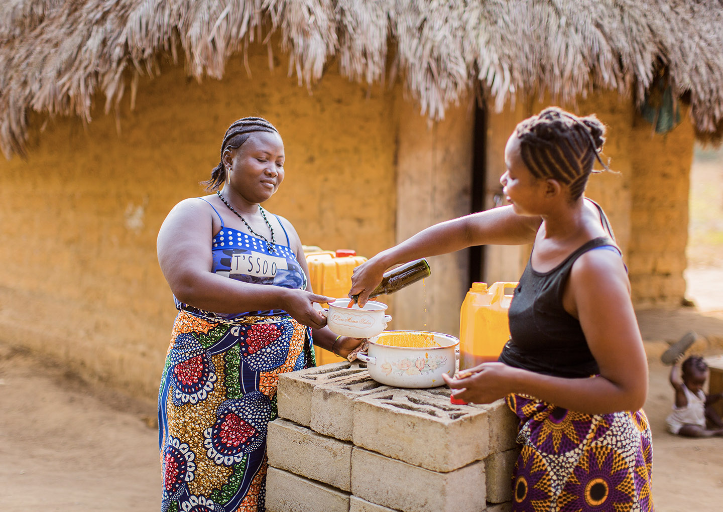 Two women stand and cook together outside, in front of a house