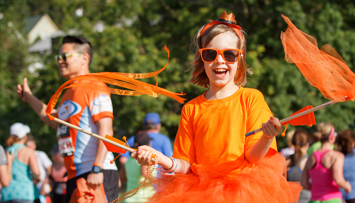 Young girl wearing an orange t-shirt, glasses and waving orange flags
