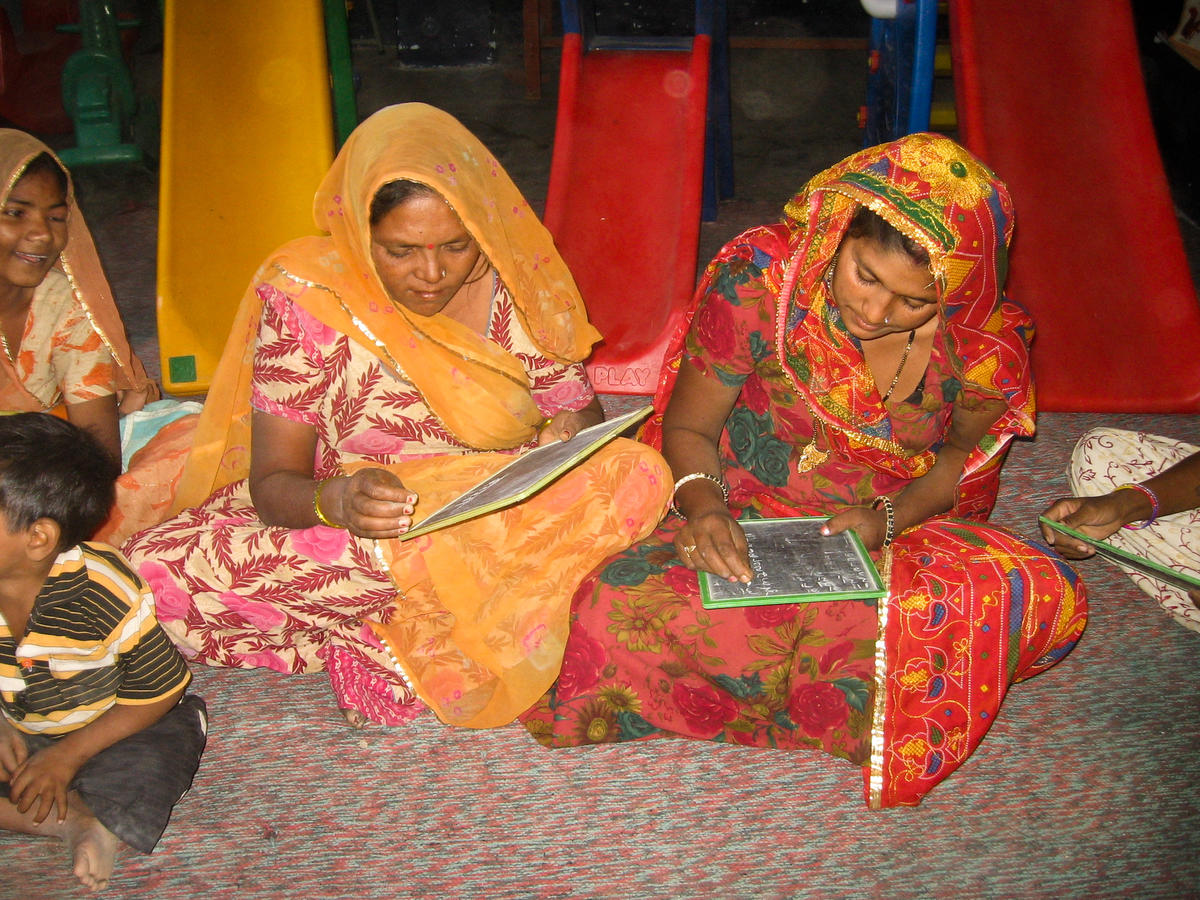 Two women in India sit together as they write