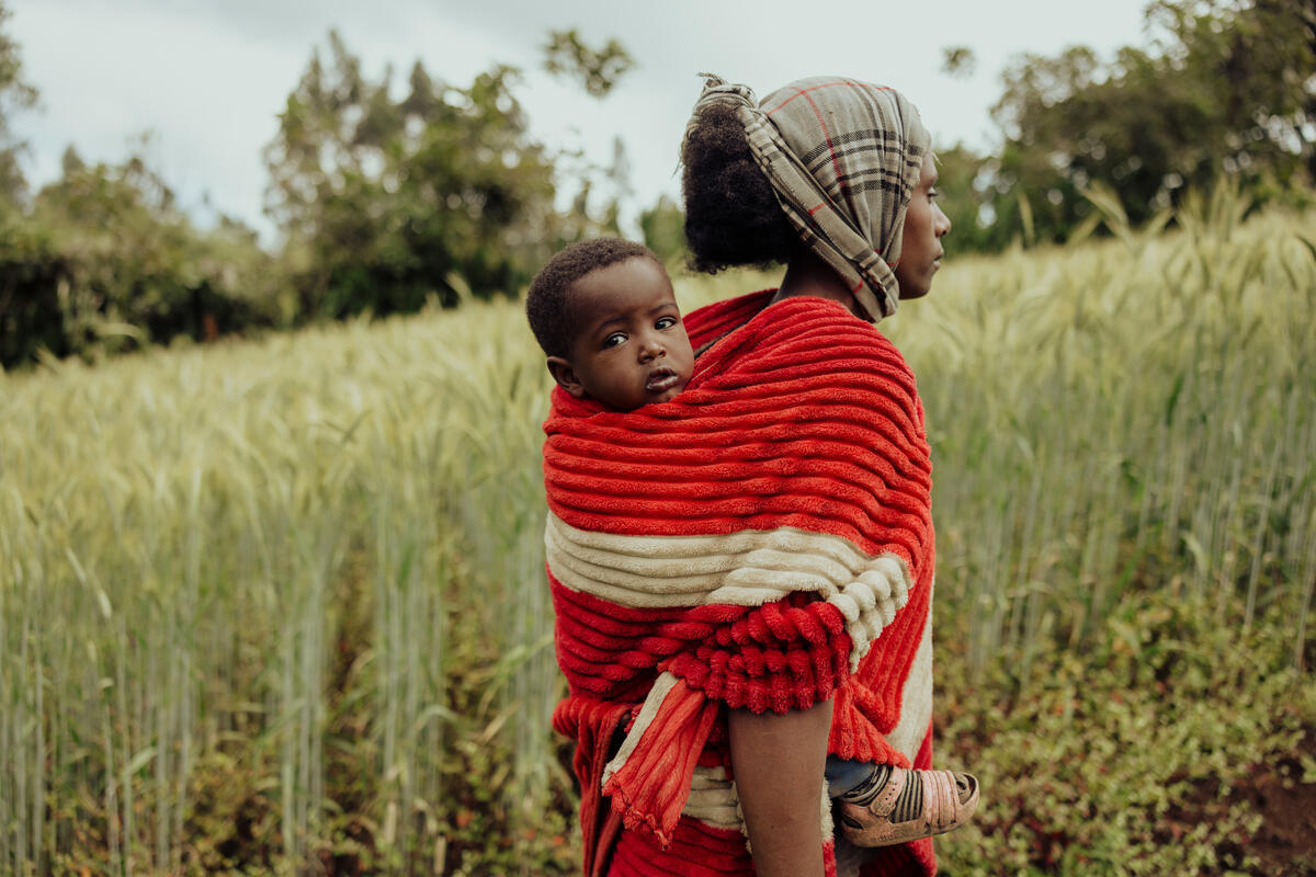 Young Ethiopian girl carries a baby on her back, she's walking in a field.