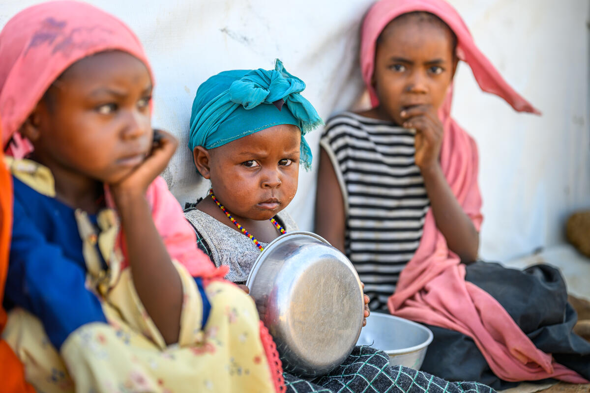 Three children are sat on the ground holding empty bowls
