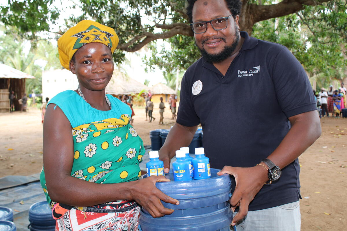 Woman from Malawi holding a water tank with World Vision staff