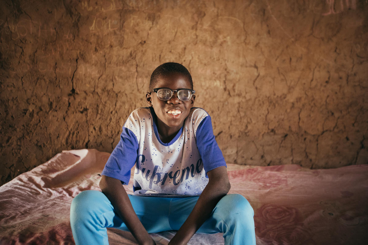 A visually impaired boy, in Senegal, sits at home on the edge of his bed, smiling