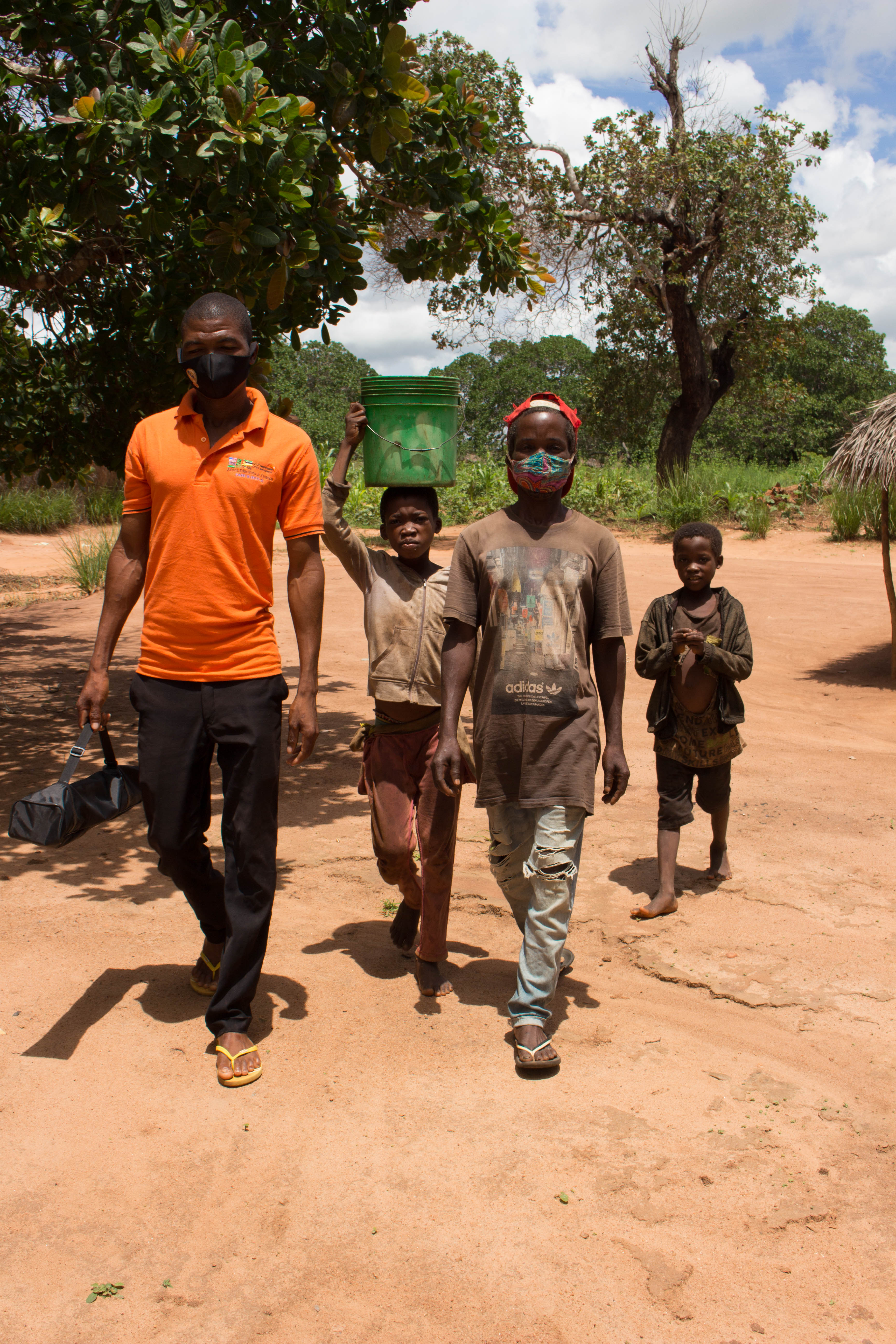 Dércio, 14, returns from the water fountain with a bucket on his head. He is in the company of his father, young brother, and a member of the Tulua Water Committee.