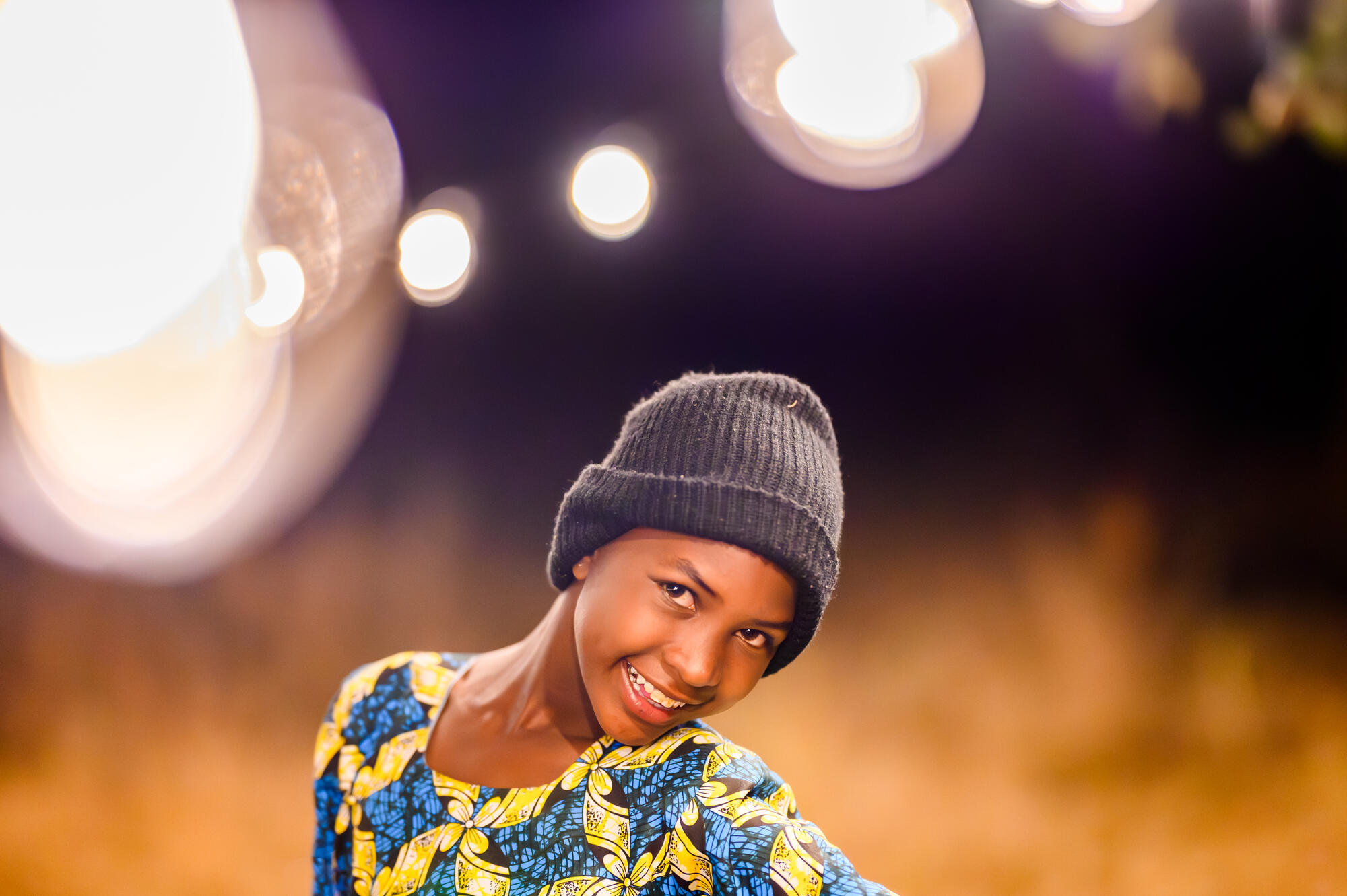 A girl in Tanzania stands in front of a dark background and soft white lights