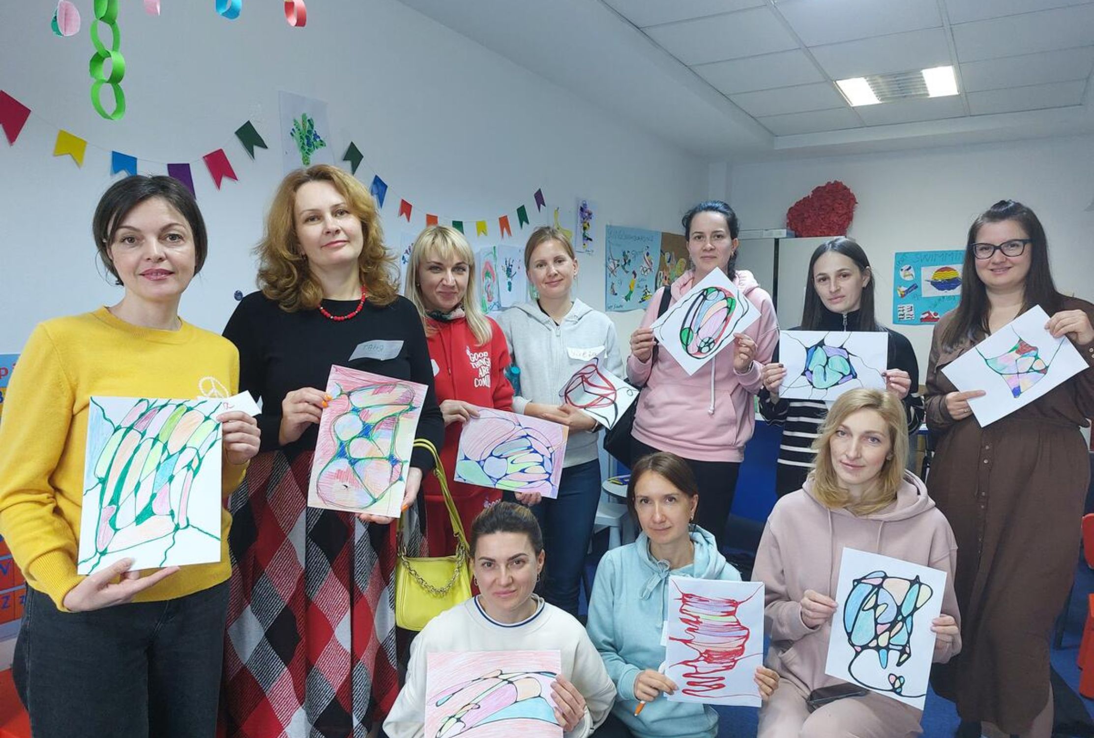 Ukrainian women holding up their art from attending a psychosocial support class in Romania