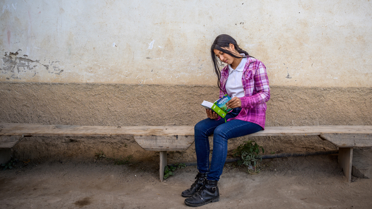 Nahomy sits outside on a bench, reading a favourite book