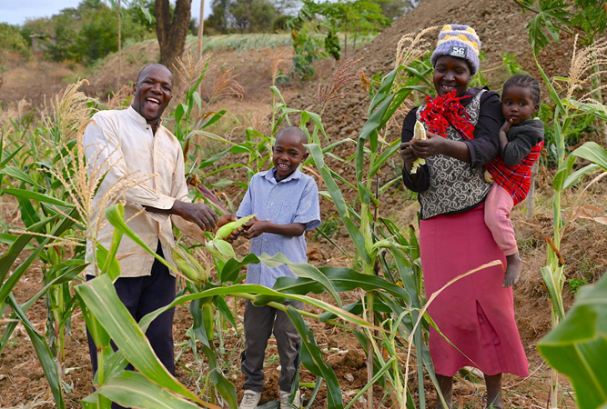 A Kenyan family standing and holding the crops they have grown