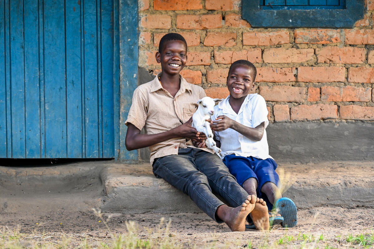 Ugandan brother sitting outside a brick house hugging a goat