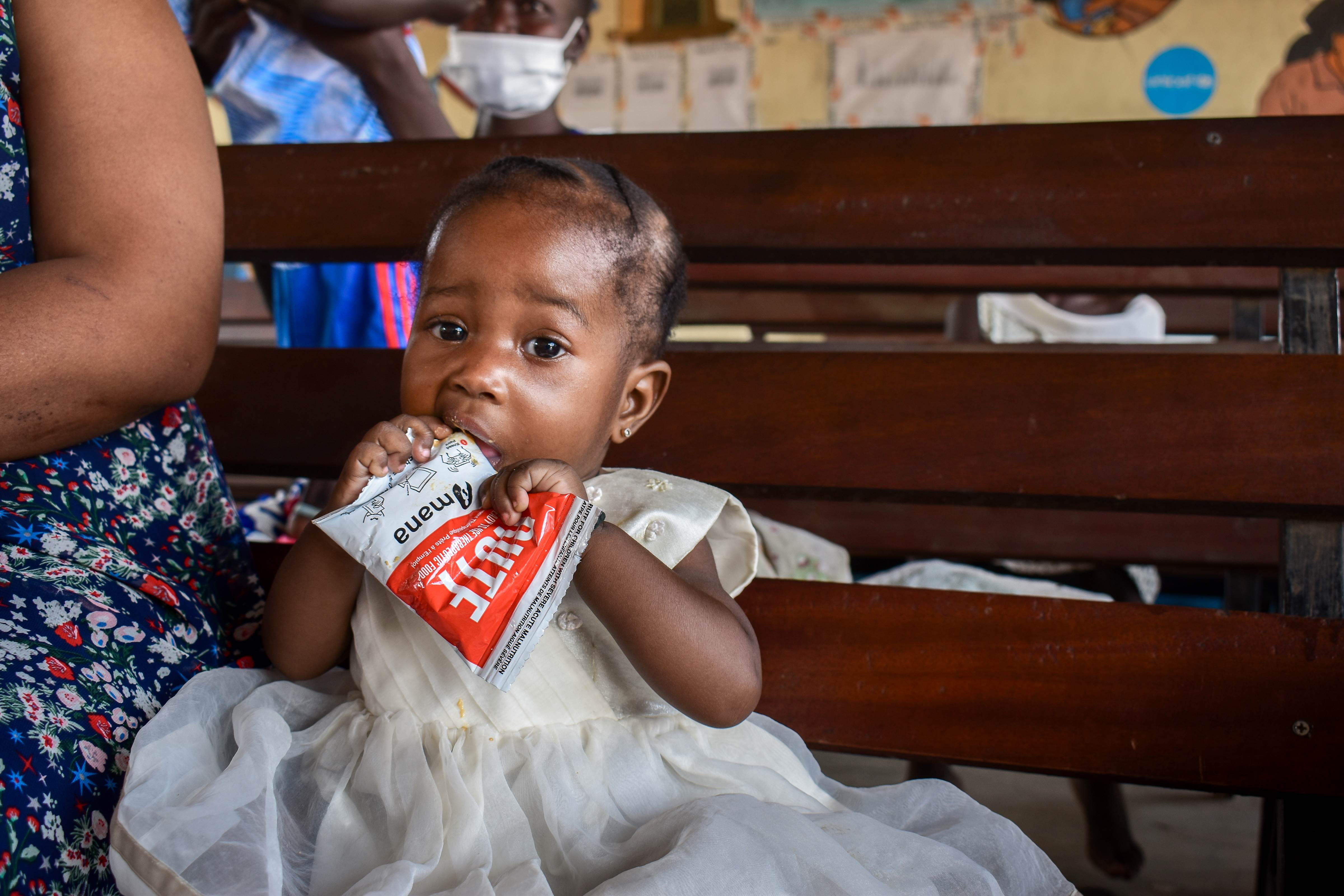 A girl sits eating from a packet of nutritious food that helps malnourished children
