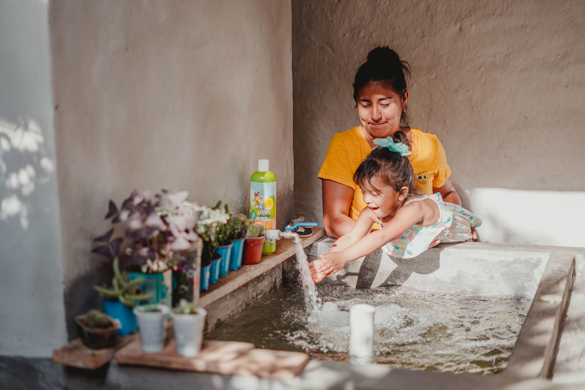 A mother holds her young daughter above a sink as the girl reaches out to run her hands under the running water form the tank.  water from a well full of dirty water and a frog