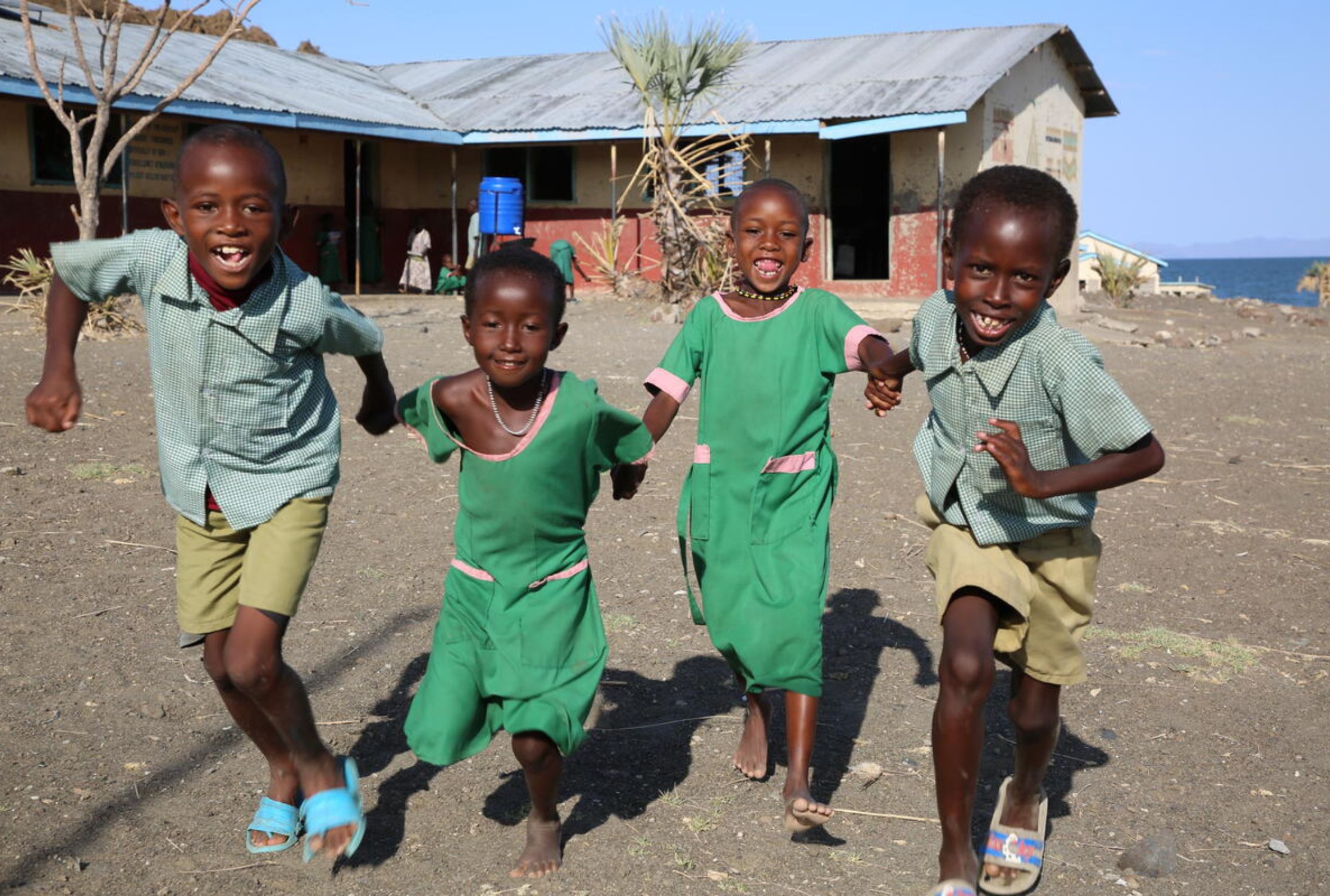 Four Kenyan school children holding hands and running towards the camera