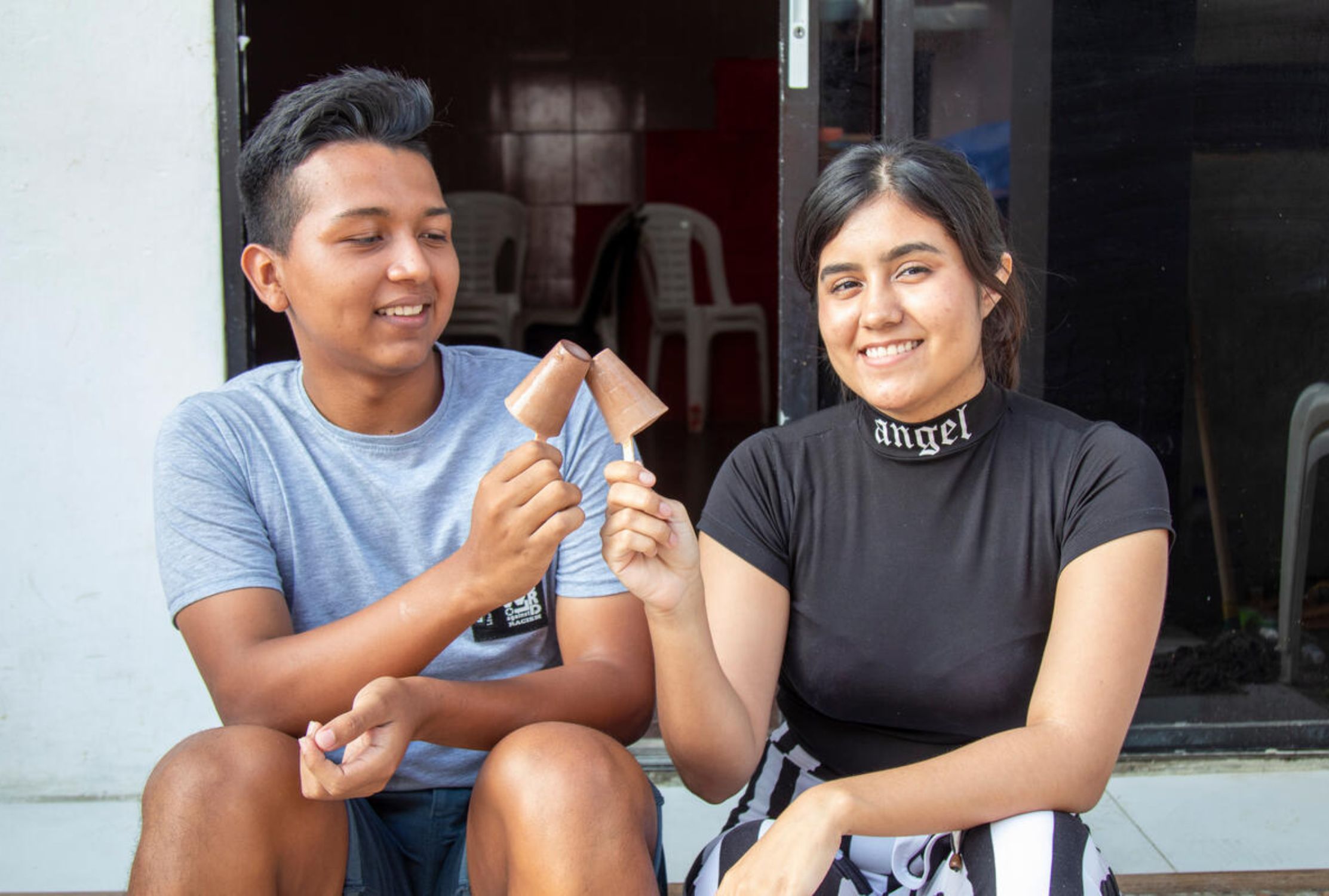 Ecuadorian boy on the left and girl on the right holding up their ice-cream and smiling